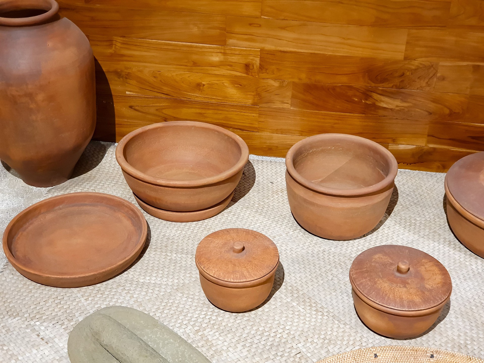 Traditional handcrafted clay pots and vessels arranged aesthetically on a woven mat in a rustic setting
